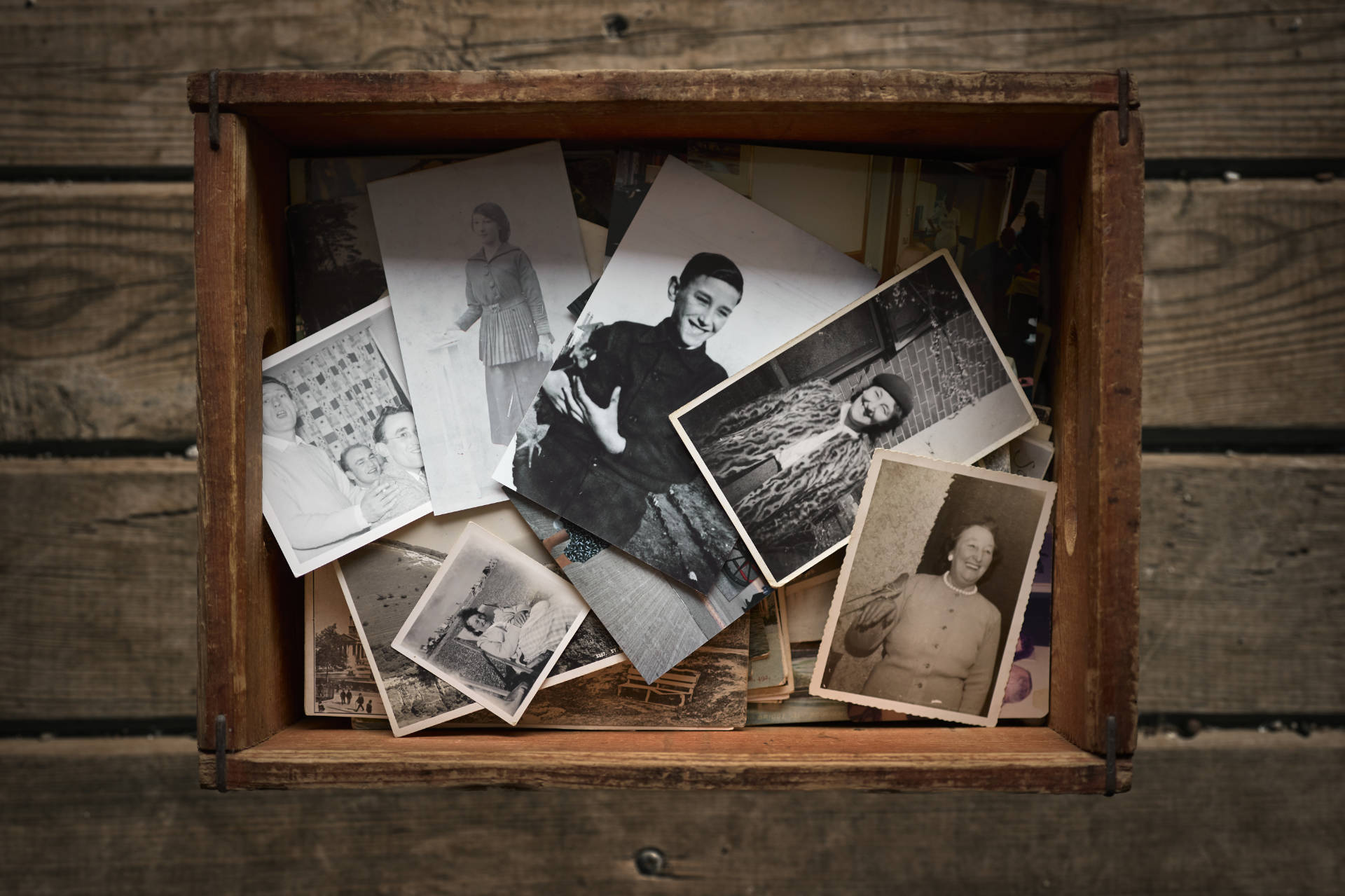 An old vintage wooden beer crate filled with vintage black and white photographs, with wooden floorboards as a background
